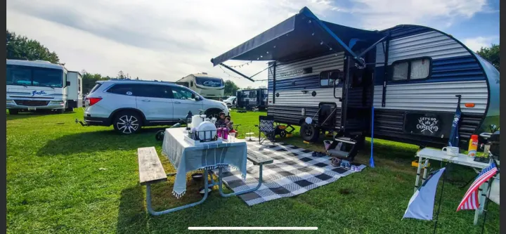 Relaxing at an RV rental campsite: a travel trailer, SUV, picnic table, and outdoor mat are set up on green grass.. Forest River Cherokee Wolf Pup 2022