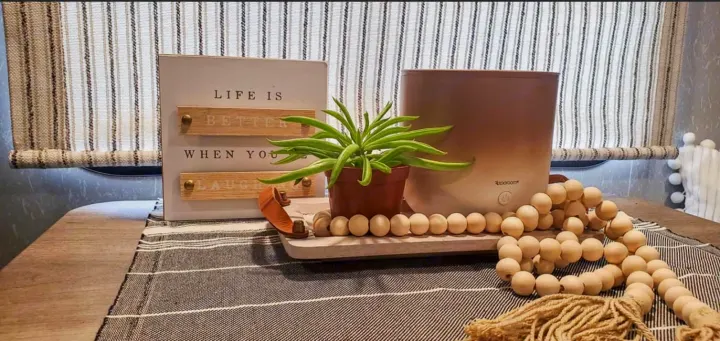 This cozy RV rental interior features thoughtful decor on a wood countertop: a "Life is Better" sign, plant, diffuser, and wood bead garland.. Forest River Cherokee Wolf Pup 2022