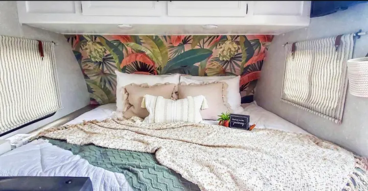 Step into this beautifully updated rv rental bedroom. Features tropical wallpaper, layered bedding, and striped window blinds.. Forest River Cherokee Wolf Pup 2022