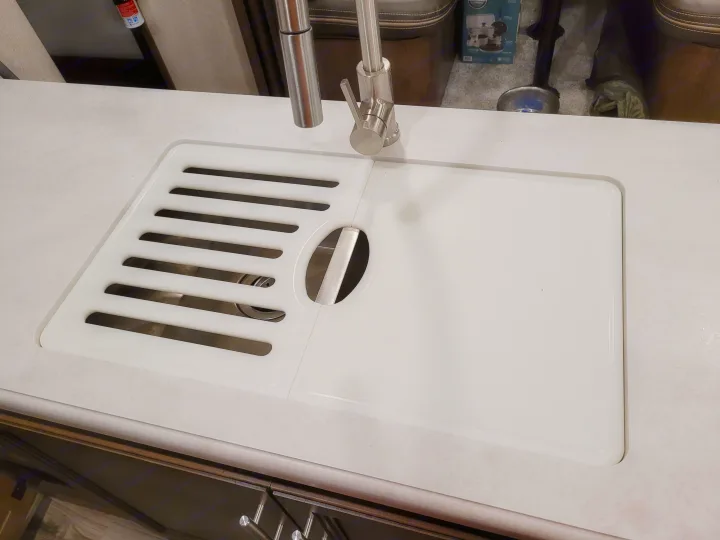 RV rental compact kitchen sink with integrated drying rack & cutting board cover, alongside a modern pull-down faucet.. Keystone RV Cougar 2020