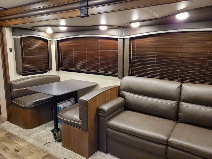 RV rental interior: cozy dinette with table and benches, plush sofa, and horizontal window blinds. Warm lighting and wood accents.. Keystone RV Cougar 2020