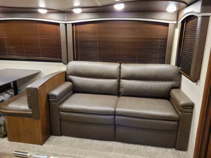Cozy RV rental interior: A living area featuring a comfortable brown sofa and dining booth with window blinds.. Keystone RV Cougar 2020
