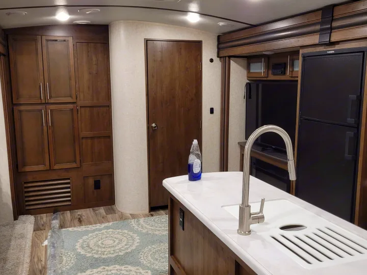 RV rental interior: A bright, modern living space with a kitchen island and sink, dark wood cabinets, and an entertainment area.. Keystone RV Cougar 2020