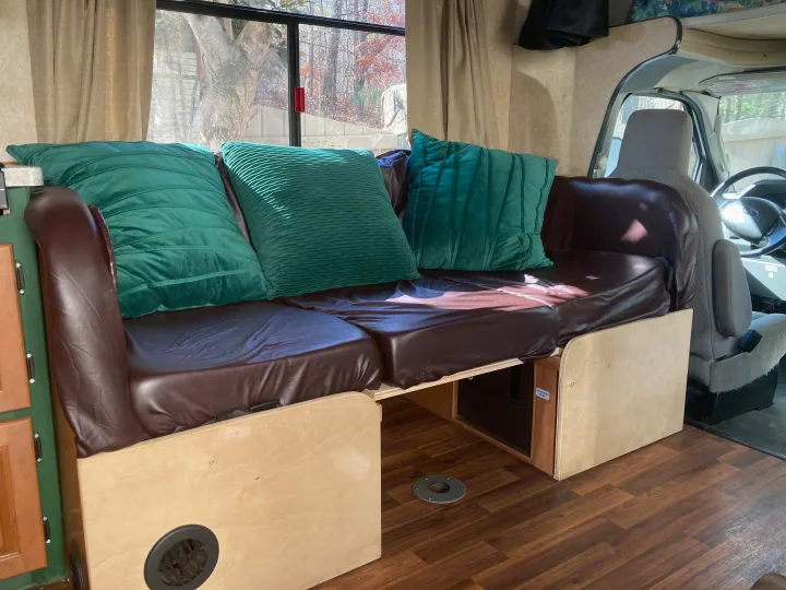 Cozy RV rental interior with a brown leather couch, green pillows, and a window view of autumn trees.. Thor Majestic 2016