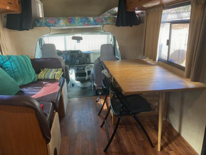 Inside a cozy RV rental: a wooden dinette, comfortable seating, overhead bed, and wood-look flooring.. Thor Majestic 2016