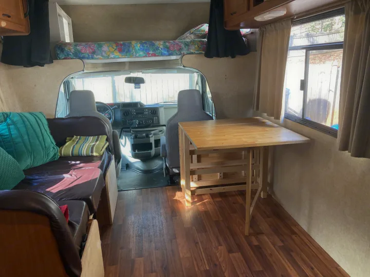Inside an RV rental: cozy overhead bunk, wood-look floor, comfortable sofa, and folding dining table. Perfect for travel!. Thor Majestic 2016