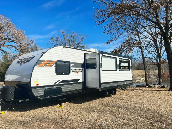 White Wildwood X-Lite travel trailer (rv rental) by a calm lake on a sunny day with autumn trees.. Forest River Wildwood X-Lite 2022