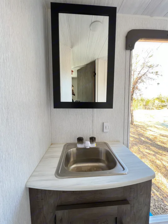 RV rental bathroom vanity with sink, mirror, and window view. Clean and functional interior.. Forest River Wildwood X-Lite 2022
