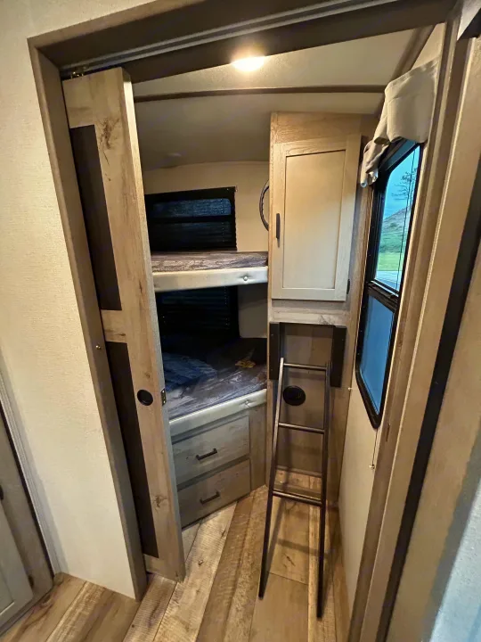 Explore this RV rental's bunk room, featuring two beds, a ladder, drawers, and a sliding privacy door.. Keystone RV Outback Ultra-Lite 2021