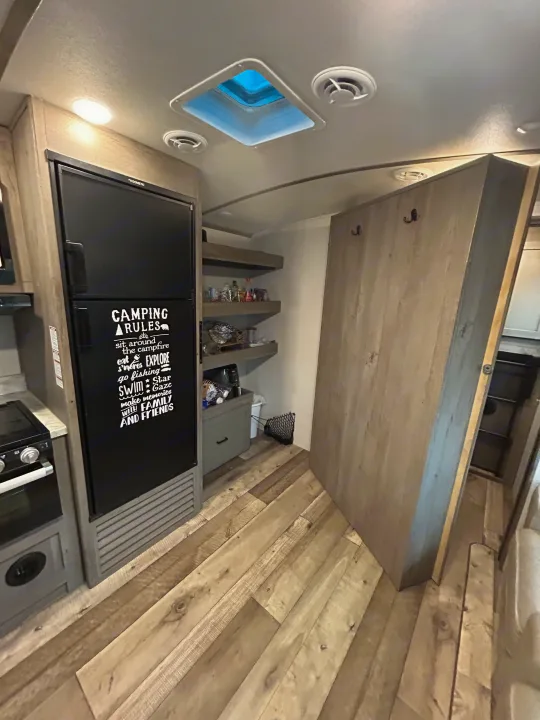 Cozy RV rental interior: kitchen with Dometic fridge, stove, shelves, and skylight. "Camping Rules" sticker adds fun to this compact space.. Keystone RV Outback Ultra-Lite 2021
