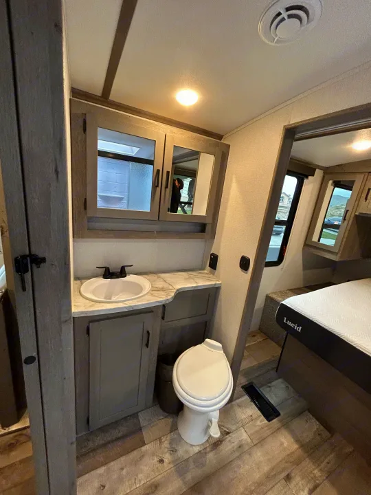 RV rental with compact bathroom: sink, toilet, medicine cabinet, and adjacent Lucid bed for a comfortable stay.. Keystone RV Outback Ultra-Lite 2021