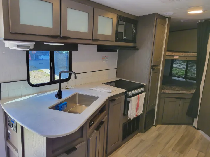 Modern RV rental interior: well-equipped kitchen with sink, stove, microwave, and comfortable bunk beds for extra sleeping space.. Cruiser RV MPG Ultra Lite 2022