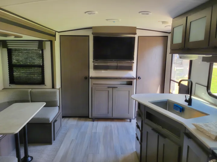 Modern RV rental interior showing a dinette, entertainment center with TV, and kitchen island with sink.. Cruiser RV MPG Ultra Lite 2022