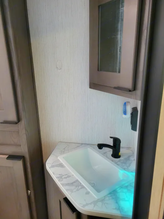 Modern compact RV rental bathroom showing sink, black faucet, and marble-look counter with blue underglow. Ready for travel.. Cruiser RV MPG Ultra Lite 2022