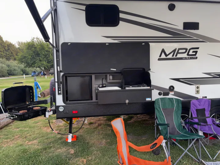 RV rental featuring a convenient outdoor kitchen with a sink, fridge, stove, and a grill cooking burgers at the campsite.. Cruiser RV MPG Ultra Lite 2022