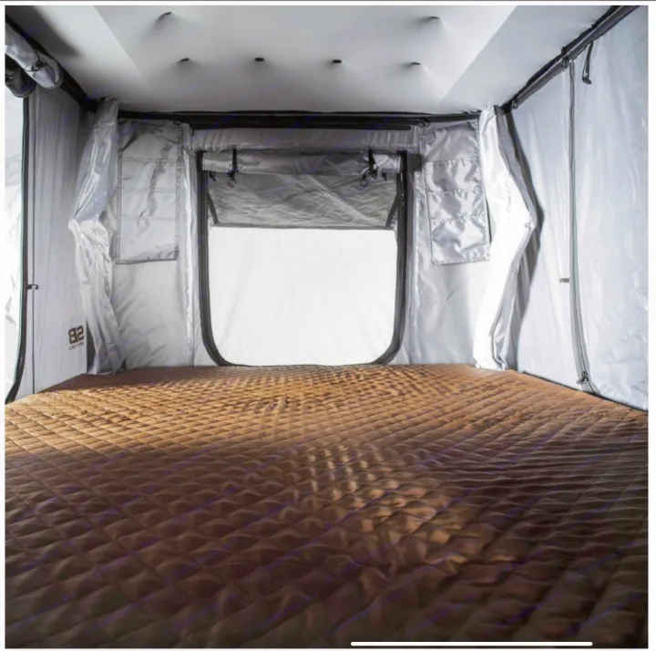 Inside a modern rv rental rooftop tent. Features a comfortable, brown quilted mattress and light fabric walls with storage.. Smittybilt Hardshell RTT 2022