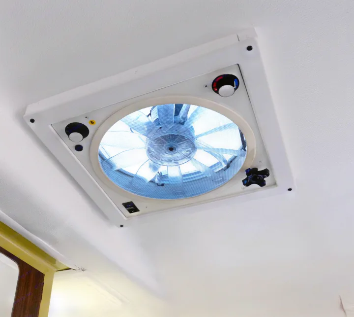 Inside an **RV rental**: a bright ceiling vent fan with visible blades, screen, and controls for air circulation.. Trillium Rv 1300 1976