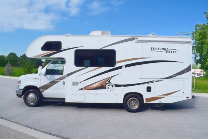 This spacious white RV rental, a Class C motorhome, is ready for your road trip adventure. Parked on asphalt under a clear sky.. Thor Freedom Elite 2016