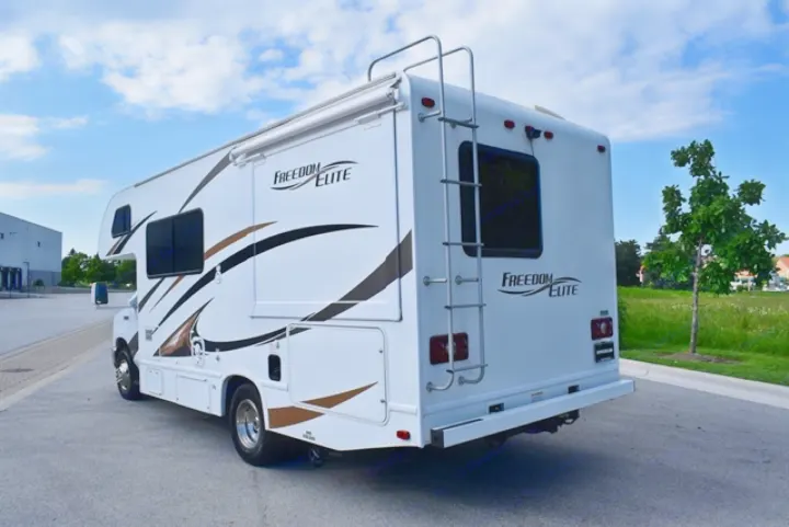 White Freedom Elite RV rental parked on asphalt, featuring a rear ladder and side awning, ideal for travel.. Thor Freedom Elite 2016