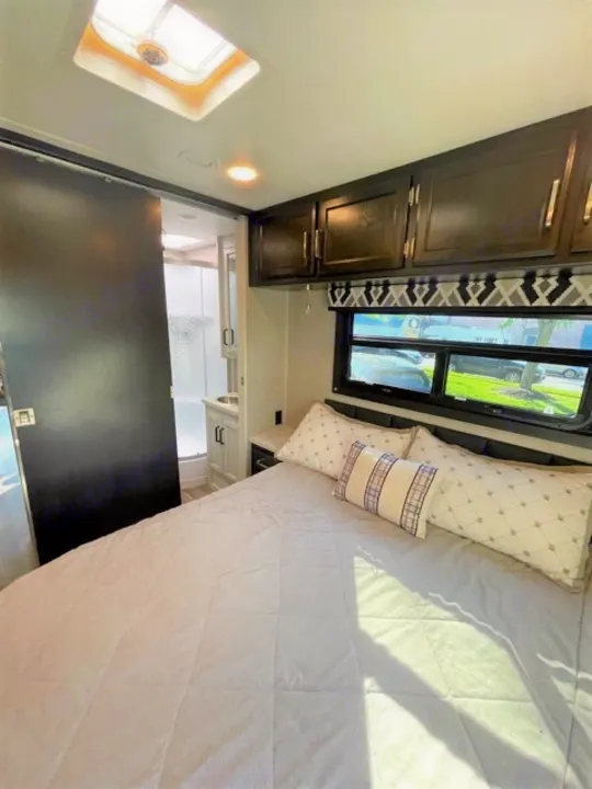 Explore this comfy RV rental bedroom! Features a large bed, overhead storage, and a connected private bathroom with a skylight.. Jayco Redhawk 2022