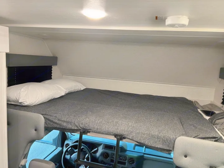 RV rental interior: A neatly made cabover bunk bed with pillows, positioned above the driver's cockpit for extra sleeping.. East to West Entrada 2600DS 2022