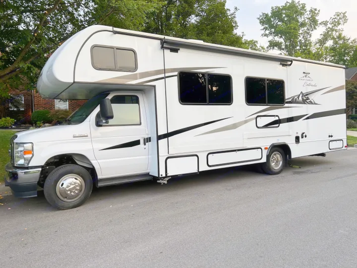 This white East to West Entrada Class C RV rental with black/grey graphics is ready for adventure, parked on a suburban street.. East to West Entrada 2600DS 2022