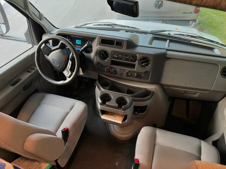 Inside this rv rental van: a detailed view of the front interior, featuring the gray dashboard, steering wheel, and comfortable bucket seats.. East to West Entrada 2600DS 2022