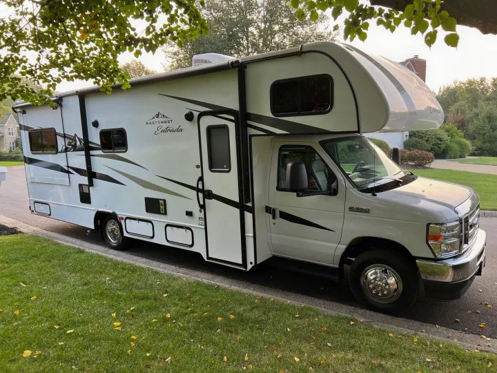 White Class C motorhome, an East◎West Entrada, ready for rv rental. Parked curbside on a sunny suburban street.. East to West Entrada 2600DS 2022
