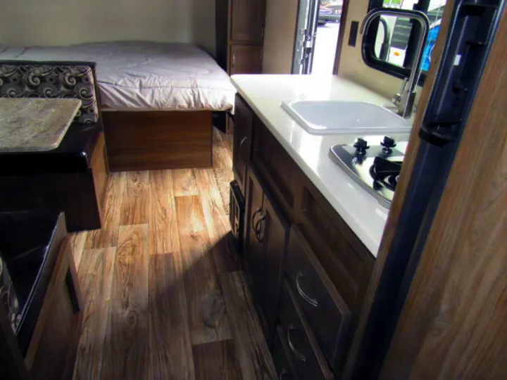 RV rental interior: compact kitchen with stove & sink, dinette, and bed area, all on wood flooring.. Riverside Rv Dream 175BH 2018