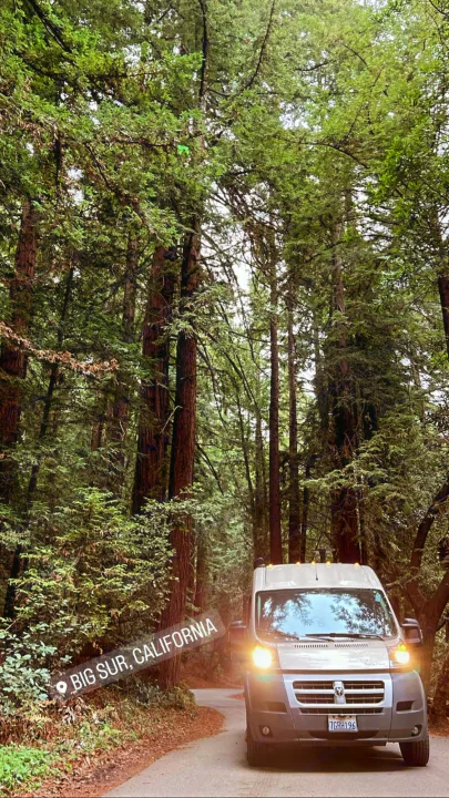 RV rental in Big Sur, California: A modern camper van with headlights on, winding through a lush, towering redwood forest.. Winnebago Travato 2014