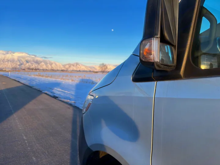 White RV rental van parked on a snowy road, showcasing majestic snow-capped mountains under a clear sky.. Winnebago Revel 2020