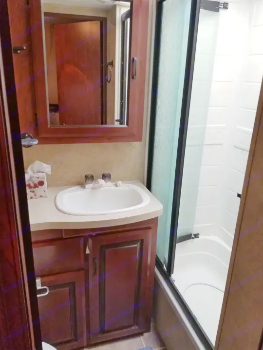 Compact RV rental bathroom features: sink vanity, mirrored cabinet, and a shower/tub combo with a frosted glass door.. Forest River Sunseeker 2013