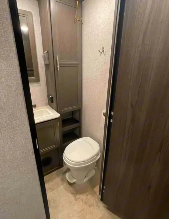 Inside a compact RV rental bathroom: features include a toilet, sink with vanity, tall storage cabinet, and mirror.. Dutchmen Kodiak SE 2021