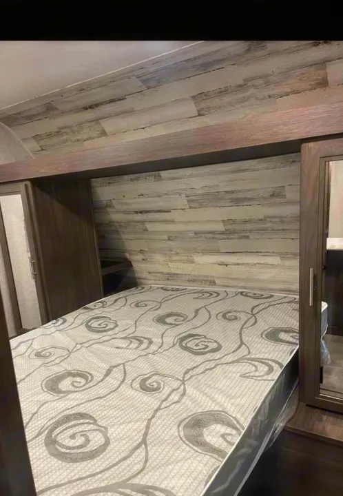 Inside an RV rental: a cozy bedroom featuring a comfortable bed, wood paneling, and built-in storage.. Dutchmen Kodiak SE 2021