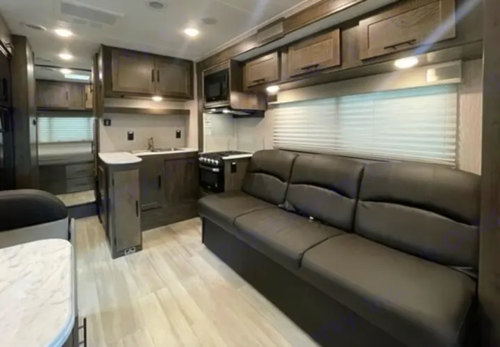 Modern RV rental interior featuring a full kitchen, comfortable black sofa, and rear sleeping area with light flooring.. Other Leprechaun 2022