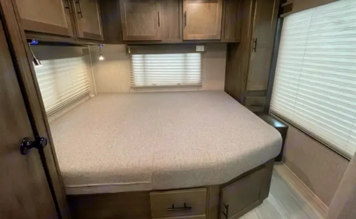 Cozy RV rental bedroom features a comfy bed, overhead storage cabinets, and bright windows with blinds for peaceful nights.. Other Leprechaun 2022