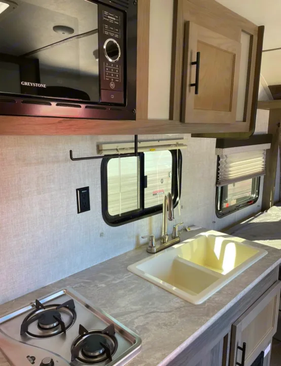 Interior of an RV rental kitchen showing a microwave, sink, two-burner stovetop, and modern light wood cabinetry.. Gulf Stream Other 2022