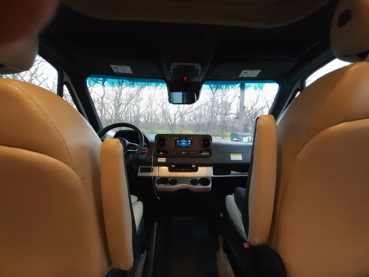 RV rental cabin: Interior view from between tan seats, showing dashboard, steering wheel, and trees through the windshield.. Thor Motor Coach Four Winds 2023