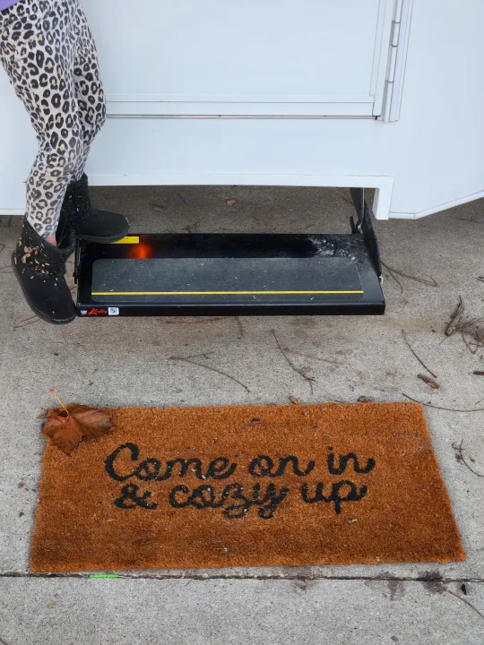 Leopard print clad legs near an RV rental with a Kwikkee step & 'Come on in & cozy up' mat. Ready for adventure!. Thor Motor Coach Four Winds 2023