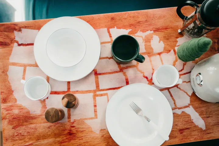 RV rental dining: white dishes, mugs, French press, and kettle on a wood table with U.S. state map outlines.. Jayco Jay 2015