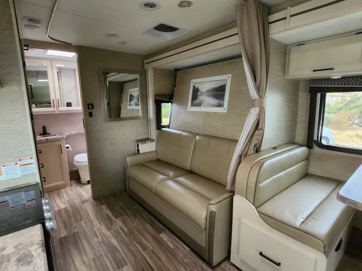 Experience comfortable living in this RV rental: Features a light-toned sofa, dinette, and visible compact bathroom.. Thor Motor Coach Four Winds 2023