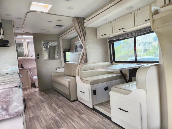 Bright RV rental interior with modern dinette, sofa, light wood-look flooring, and ample storage.. Thor Motor Coach Four Winds 2023