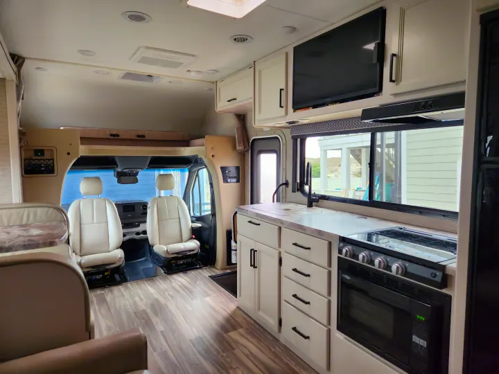 Spacious RV rental interior with a modern kitchen, comfortable cockpit, and over-cab bunk living area.. Thor Motor Coach Four Winds 2023
