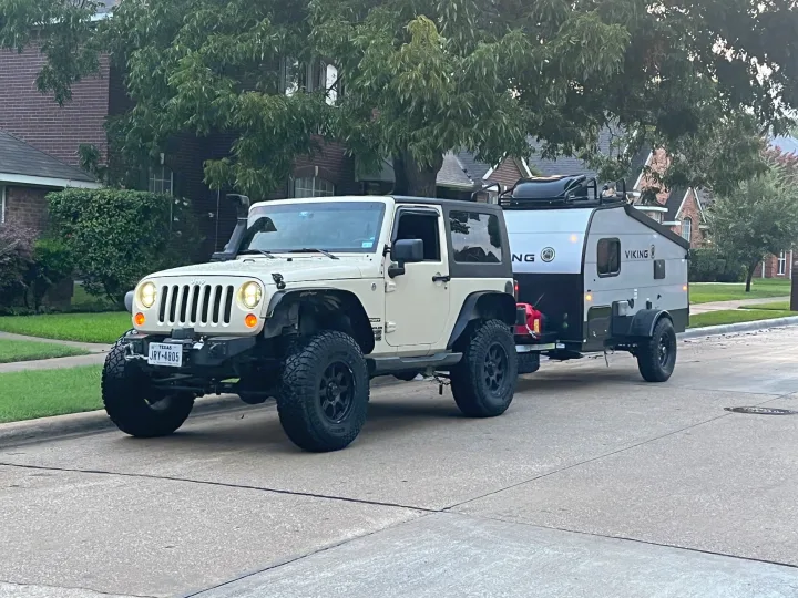 White Jeep Wrangler towing a gray Viking RV rental trailer on a suburban street, ready for adventure.. Forest River Viking TD 2022