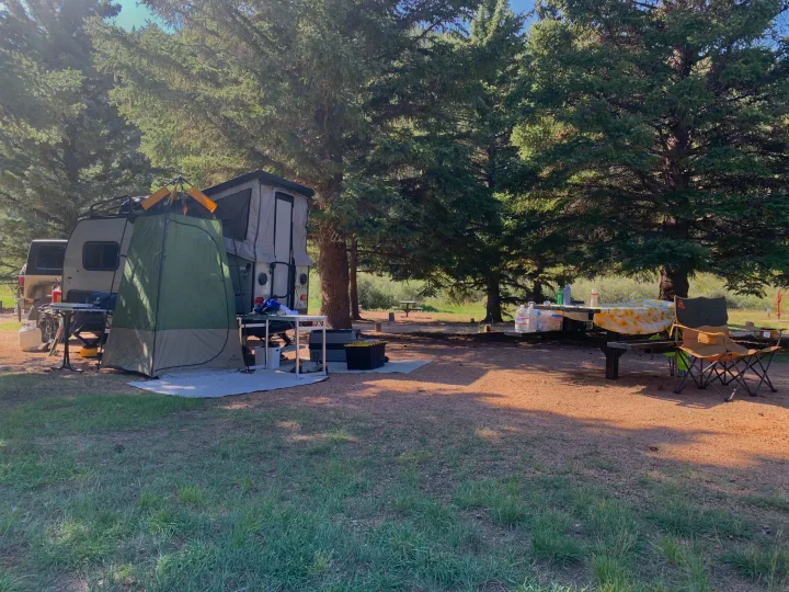 Relaxing RV rental campsite. Features a pop-up trailer with a privacy tent, picnic table, and chairs shaded by tall trees.. Forest River Viking TD 2022