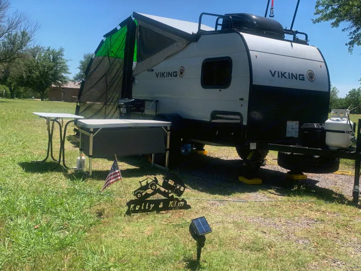 A light-colored Viking RV rental is set up for outdoor living, featuring an awning, grill, and prep table, under a clear sky.. Forest River Viking TD 2022