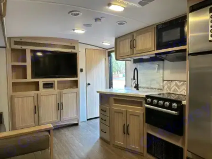 Modern RV rental interior with full kitchen (stove, microwave, fridge) and light wood living area with TV.. Twilight RVS Signature 2022