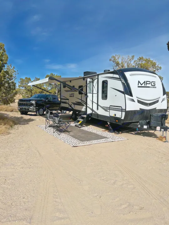 This rv rental offers a comfy outdoor setup! A truck, travel trailer, chairs & mat are ready at a sandy campsite.. Cruiser RV MPG Ultra Lite 2500BH 2021