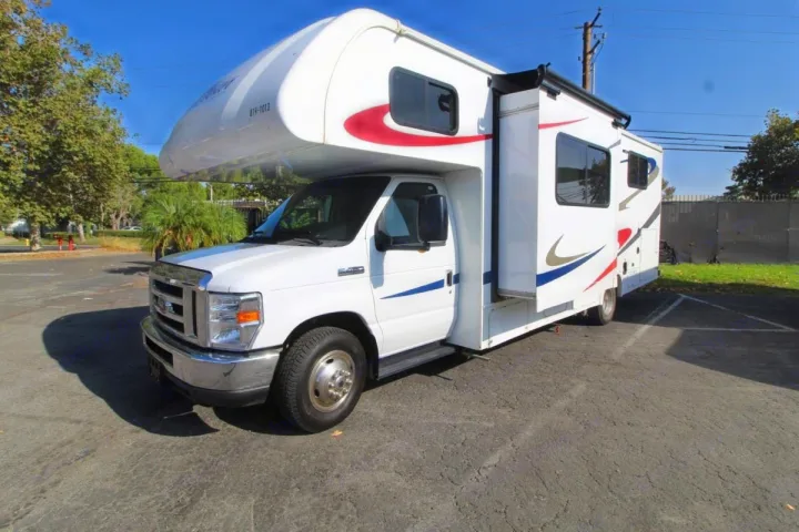 Modern white Class C RV rental with a side slide-out extended, parked on asphalt outdoors under a blue sky.. Forest River Sunseeker 2019