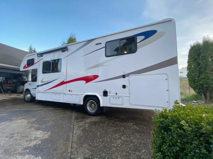 A clean, white RV rental with bold red and blue decals, parked on a driveway, ready for new adventures.. Forest River Sunseeker 2019